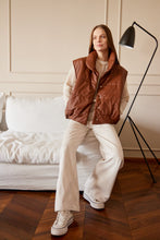 Cargar imagen en el visor de la galería, Chaleco Puffer en color Café. Diseño alcochado en cuero sintético. Tejido técnico repelente al agua. Cuello subido y sin mangas. Bolsillos laterales. Cierre frontal con botones a presión ocultos por la solapa. Forro interior con estampado de Flint. Disponible en color Café y Negro.. Productoo hecho en Colombia. Compra Online