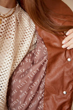 Cargar imagen en el visor de la galería, Chaleco Puffer en color Café. Diseño alcochado en cuero sintético. Tejido técnico repelente al agua. Cuello subido y sin mangas. Bolsillos laterales. Cierre frontal con botones a presión ocultos por la solapa. Forro interior con estampado de Flint. Disponible en color Café y Negro.. Productoo hecho en Colombia. Compra Online