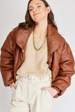 Cargar imagen en el visor de la galería, Chaqueta Puffer de mujer. Diseño alcochado en cuero sintético. Tejido técnico repelente al agua. Cuero Vegano. Cuello subido y manga larga con puños elásticos. Bolsillos laterales. Cierre frontal con botones a presión ocultos por la solapa. Forro interior con estampado de Flint. Disponible en color Café y Negro. Producto 100% hecho en Colombia.