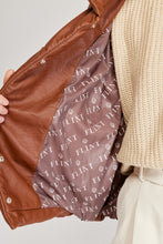 Cargar imagen en el visor de la galería, Chaqueta Puffer de mujer. Diseño alcochado en cuero sintético. Tejido técnico repelente al agua. Cuero Vegano. Cuello subido y manga larga con puños elásticos. Bolsillos laterales. Cierre frontal con botones a presión ocultos por la solapa. Forro interior con estampado de Flint. Disponible en color Café y Negro. Producto 100% hecho en Colombia.