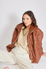 Cargar imagen en el visor de la galería, Chaqueta Puffer de mujer. Diseño alcochado en cuero sintético. Tejido técnico repelente al agua. Cuero Vegano. Cuello subido y manga larga con puños elásticos. Bolsillos laterales. Cierre frontal con botones a presión ocultos por la solapa. Forro interior con estampado de Flint. Disponible en color Café y Negro. Producto 100% hecho en Colombia.