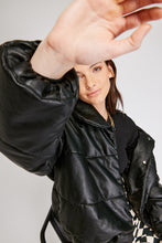 Cargar imagen en el visor de la galería, Chaqueta Puffer de mujer. Diseño alcochado en cuero sintético. Tejido técnico repelente al agua. Cuero Vegano. Cuello subido y manga larga con puños elásticos. Bolsillos laterales. Cierre frontal con botones a presión ocultos por la solapa. Forro interior con estampado de Flint. Disponible en color Café y Negro. Producto 100% hecho en Colombia.