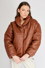 Cargar imagen en el visor de la galería, Chaqueta Puffer de mujer. Diseño alcochado en cuero sintético. Tejido técnico repelente al agua. Cuero Vegano. Cuello subido y manga larga con puños elásticos. Bolsillos laterales. Cierre frontal con botones a presión ocultos por la solapa. Forro interior con estampado de Flint. Disponible en color Café y Negro. Producto 100% hecho en Colombia.