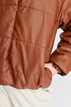 Cargar imagen en el visor de la galería, Chaqueta Puffer de mujer. Diseño alcochado en cuero sintético. Tejido técnico repelente al agua. Cuero Vegano. Cuello subido y manga larga con puños elásticos. Bolsillos laterales. Cierre frontal con botones a presión ocultos por la solapa. Forro interior con estampado de Flint. Disponible en color Café y Negro. Producto 100% hecho en Colombia.