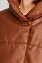 Cargar imagen en el visor de la galería, Chaqueta Puffer de mujer. Diseño alcochado en cuero sintético. Tejido técnico repelente al agua. Cuero Vegano. Cuello subido y manga larga con puños elásticos. Bolsillos laterales. Cierre frontal con botones a presión ocultos por la solapa. Forro interior con estampado de Flint. Disponible en color Café y Negro. Producto 100% hecho en Colombia.