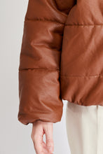 Cargar imagen en el visor de la galería, Chaqueta Puffer de mujer. Diseño alcochado en cuero sintético. Tejido técnico repelente al agua. Cuero Vegano. Cuello subido y manga larga con puños elásticos. Bolsillos laterales. Cierre frontal con botones a presión ocultos por la solapa. Forro interior con estampado de Flint. Disponible en color Café y Negro. Producto 100% hecho en Colombia.