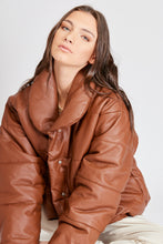 Cargar imagen en el visor de la galería, Chaqueta Puffer de mujer. Diseño alcochado en cuero sintético. Tejido técnico repelente al agua. Cuero Vegano. Cuello subido y manga larga con puños elásticos. Bolsillos laterales. Cierre frontal con botones a presión ocultos por la solapa. Forro interior con estampado de Flint. Disponible en color Café y Negro. Producto 100% hecho en Colombia.