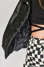 Cargar imagen en el visor de la galería, Chaqueta Puffer de mujer. Diseño alcochado en cuero sintético. Tejido técnico repelente al agua. Cuero Vegano. Cuello subido y manga larga con puños elásticos. Bolsillos laterales. Cierre frontal con botones a presión ocultos por la solapa. Forro interior con estampado de Flint. Disponible en color Café y Negro. Producto 100% hecho en Colombia.