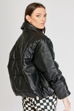 Cargar imagen en el visor de la galería, Chaqueta Puffer de mujer. Diseño alcochado en cuero sintético. Tejido técnico repelente al agua. Cuero Vegano. Cuello subido y manga larga con puños elásticos. Bolsillos laterales. Cierre frontal con botones a presión ocultos por la solapa. Forro interior con estampado de Flint. Disponible en color Café y Negro. Producto 100% hecho en Colombia.