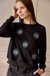 Saco con ojos de protección bordados. Tejido de algodón. Con detalle de ojos bordados. Diseño recto. Cuello redondo. Manga Larga. Cuello pretina y puños en rib tejido tono a tono. Disponible en color Negro. Porducto hecho en Colombia. Compra Online.