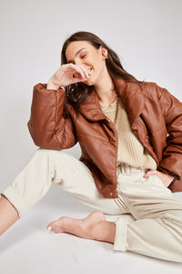 Chaqueta Puffer de mujer. Diseño alcochado en cuero sintético. Tejido técnico repelente al agua. Cuero Vegano. Cuello subido y manga larga con puños elásticos. Bolsillos laterales. Cierre frontal con botones a presión ocultos por la solapa. Forro interior con estampado de Flint. Disponible en color Café y Negro.  Producto 100% hecho en Colombia.