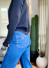 Cargar imagen en el visor de la galería, Jeans setenteros  de mujer Flint, bota campana. Tejido algodón. Modelo bota Campana. Tiro alto. Cuatro bolsillos. Cierre de cremallera y botón. Diseño azul oscuro y Bordado Happy y smiling face en uno de los bolsillos traseros. Producto 100% hecho en Colombia. Compra online
