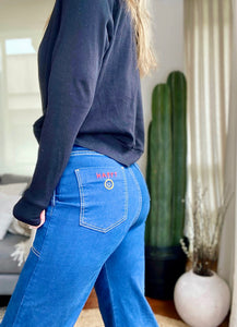 Jeans setenteros  de mujer Flint, bota campana. Tejido algodón. Modelo bota Campana. Tiro alto. Cuatro bolsillos. Cierre de cremallera y botón. Diseño azul oscuro y Bordado Happy y smiling face en uno de los bolsillos traseros. Producto 100% hecho en Colombia. Compra online