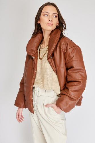 Chaqueta Puffer de mujer. Diseño alcochado en cuero sintético. Tejido técnico repelente al agua. Cuero Vegano. Cuello subido y manga larga con puños elásticos. Bolsillos laterales. Cierre frontal con botones a presión ocultos por la solapa. Forro interior con estampado de Flint. Disponible en color Café y Negro.  Producto 100% hecho en Colombia.