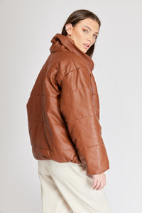 Chaqueta Puffer de mujer. Diseño alcochado en cuero sintético. Tejido técnico repelente al agua. Cuero Vegano. Cuello subido y manga larga con puños elásticos. Bolsillos laterales. Cierre frontal con botones a presión ocultos por la solapa. Forro interior con estampado de Flint. Disponible en color Café y Negro.  Producto 100% hecho en Colombia.