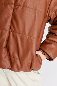 Chaqueta Puffer de mujer. Diseño alcochado en cuero sintético. Tejido técnico repelente al agua. Cuero Vegano. Cuello subido y manga larga con puños elásticos. Bolsillos laterales. Cierre frontal con botones a presión ocultos por la solapa. Forro interior con estampado de Flint. Disponible en color Café y Negro.  Producto 100% hecho en Colombia.