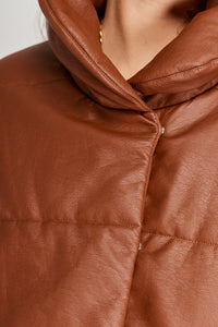 Chaqueta Puffer de mujer. Diseño alcochado en cuero sintético. Tejido técnico repelente al agua. Cuero Vegano. Cuello subido y manga larga con puños elásticos. Bolsillos laterales. Cierre frontal con botones a presión ocultos por la solapa. Forro interior con estampado de Flint. Disponible en color Café y Negro.  Producto 100% hecho en Colombia.