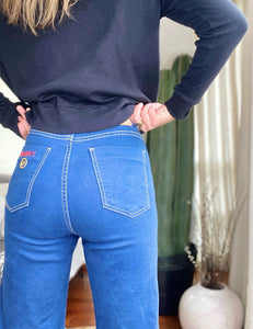 Jeans setenteros  de mujer Flint, bota campana. Tejido algodón. Modelo bota Campana. Tiro alto. Cuatro bolsillos. Cierre de cremallera y botón. Diseño azul oscuro y Bordado Happy y smiling face en uno de los bolsillos traseros. Producto 100% hecho en Colombia. Compra online